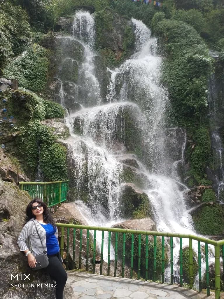 A traveler posing beside the cascading mountain waterfall framed by green bamboo railings in Gangtok, Sikkim