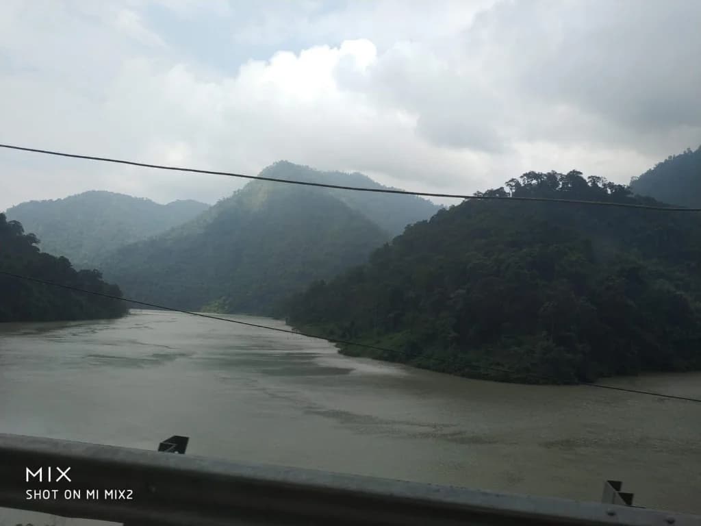 A wide view of the Teesta River flowing through lush green hills under a cloudy sky