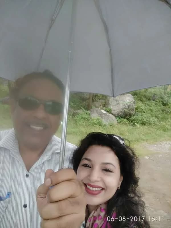 Wanderers smiling under a grey umbrella during rainfall at Neugal Khad