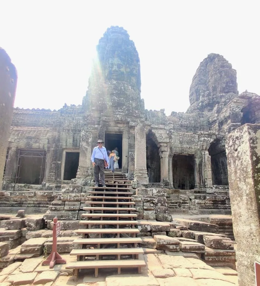 Man standing on wooden stairs leading up to Bayon temple