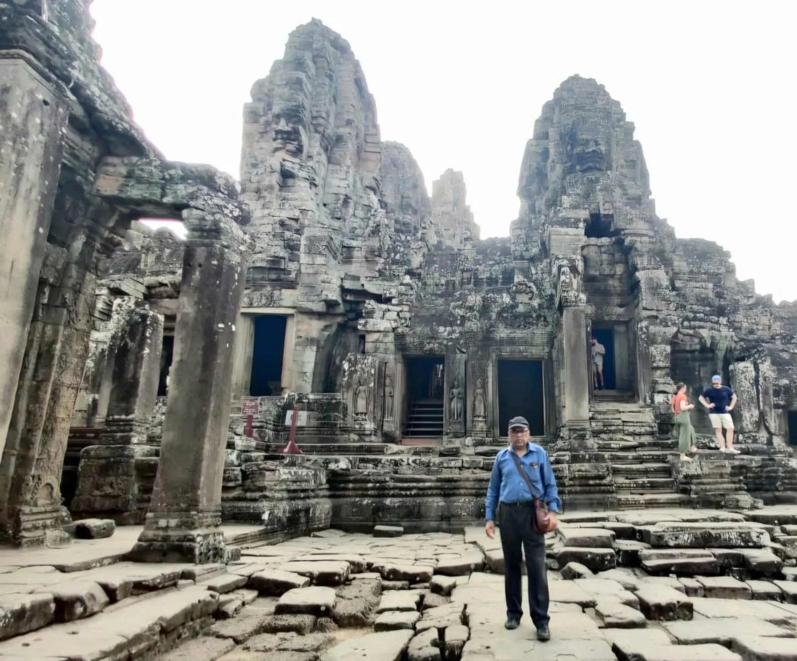 Man posing in front of the massive stone towers with carved faces at Bayon temple
