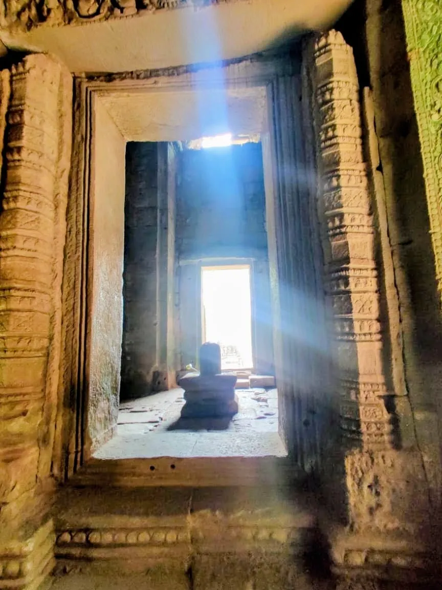 Sunrays shining through an ancient doorway onto a small Shiva linga