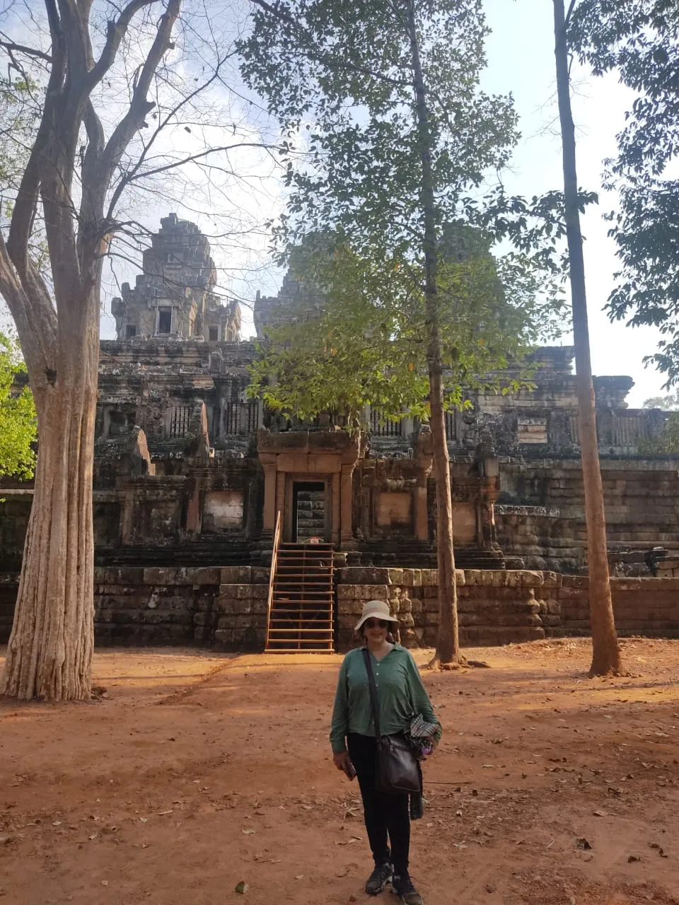 Woman standing near wooden stairs leading up to an ancient stone temple structure surrounded by trees