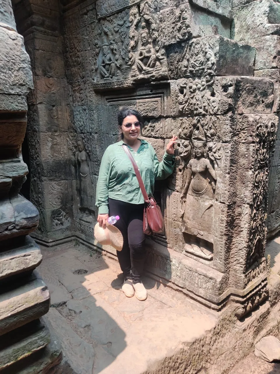 Woman standing next to a carved stone relief of an apsara at Bayon