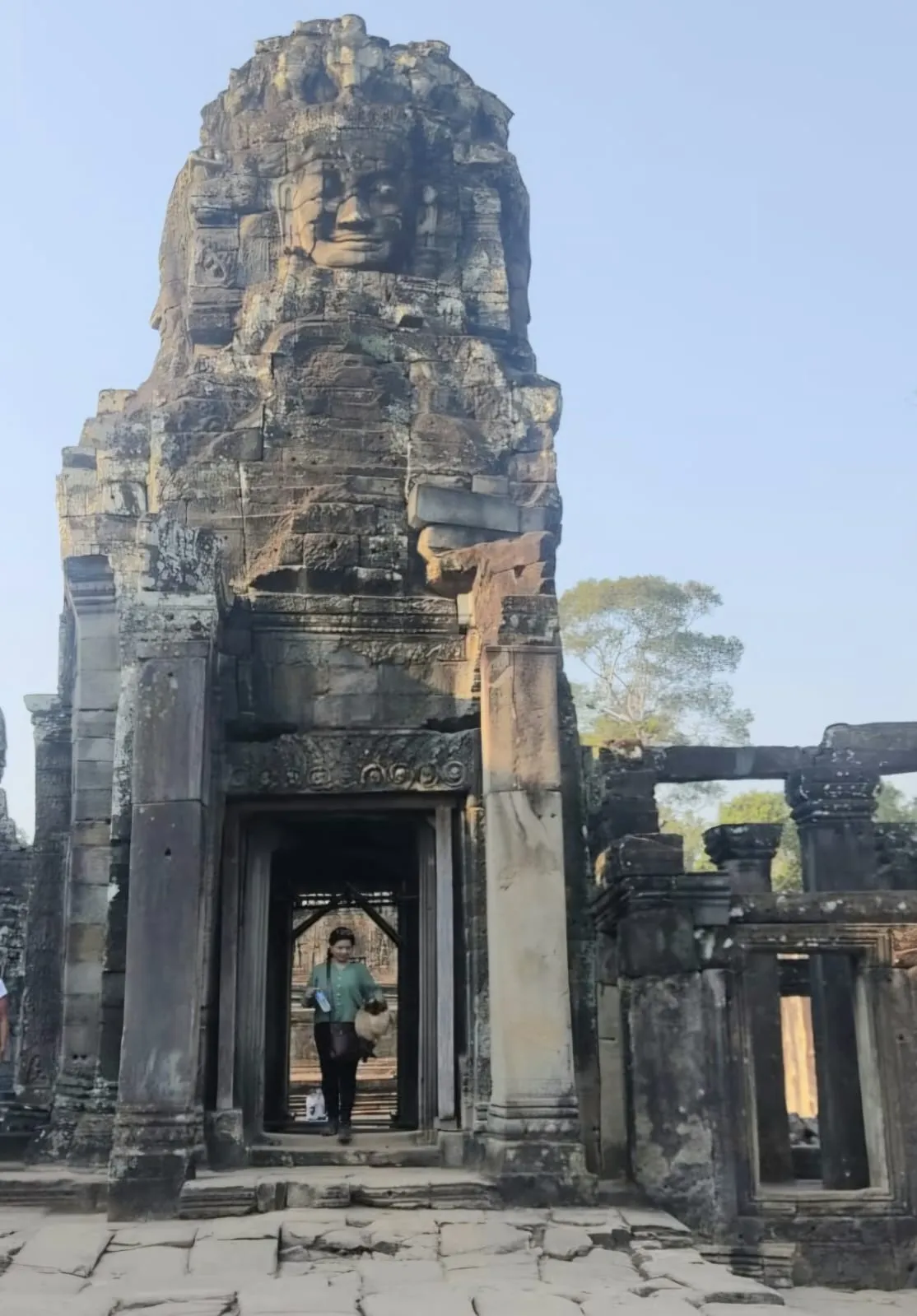 Woman walking through an ancient doorway at Bayon temple under a stone tower