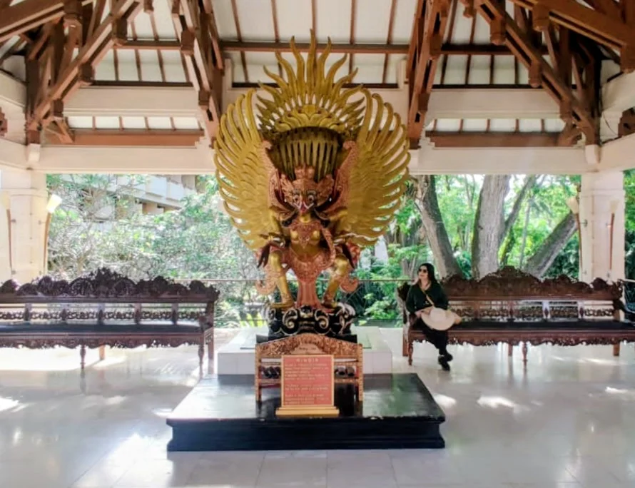 Traveler seated in pavilion lobby before the magnificent golden winged Garuda statue