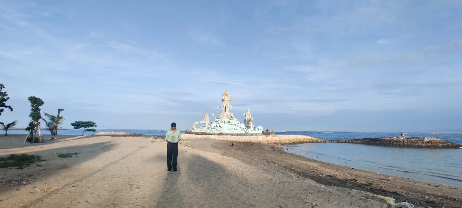 Traveler on the beach with the majestic statue of Varuna watching over the Bali coastline
