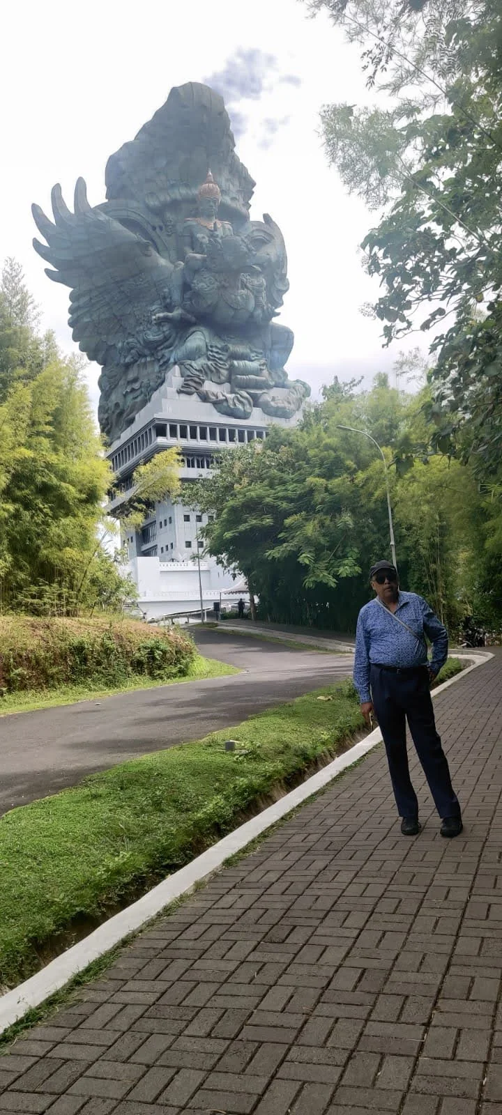 Traveler on the pathway looking up at the monumental 120-meter GWK statue rising above the trees in Bali