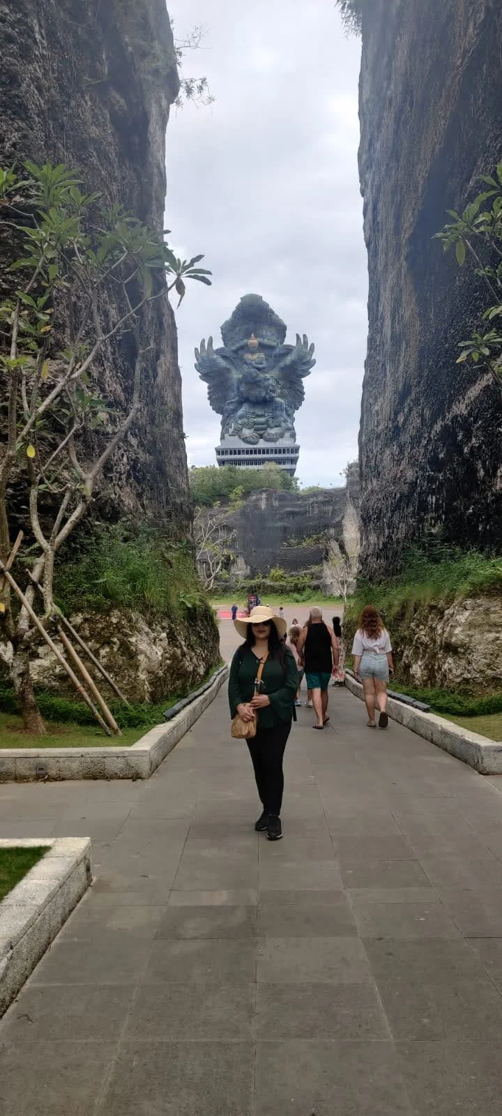 Archana walking through the towering limestone canyon corridor with the colossal GWK monument perfectly centered