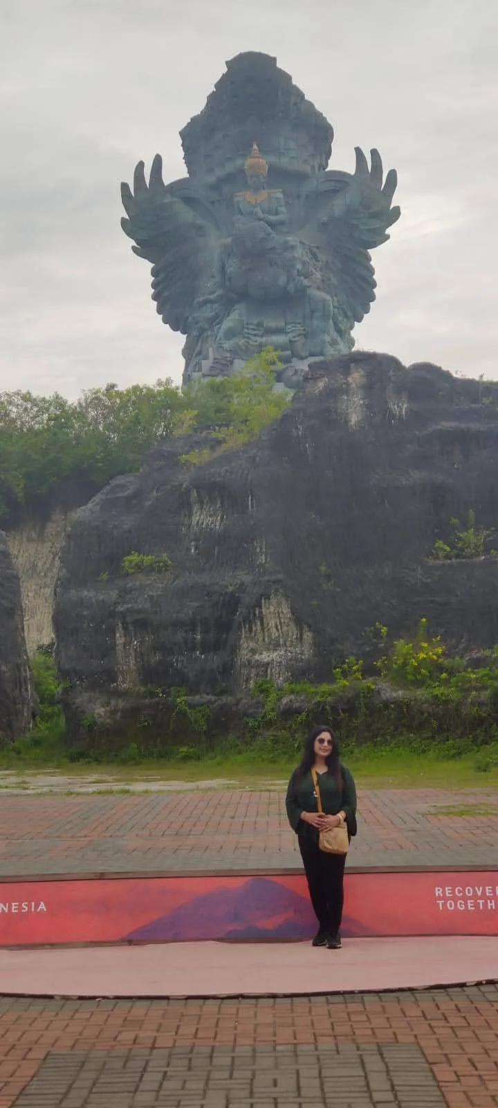 Archana standing in the grand courtyard with GWK statue atop the limestone plateau