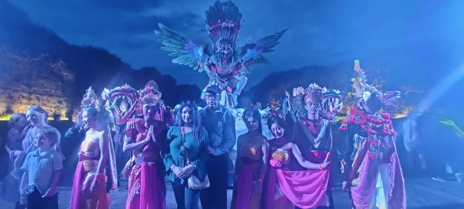 Travelers centered with the theatrical night cast of Garuda Wisnu Kencana against illuminated cliffs in Bali