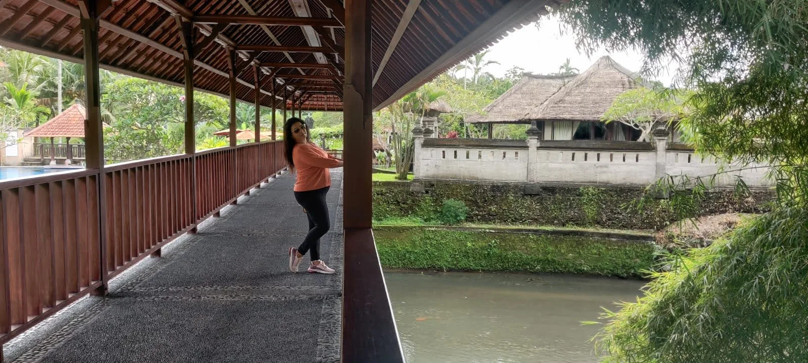 Traveler inside the covered wooden bridge spanning the river stream at the Balinese village resort