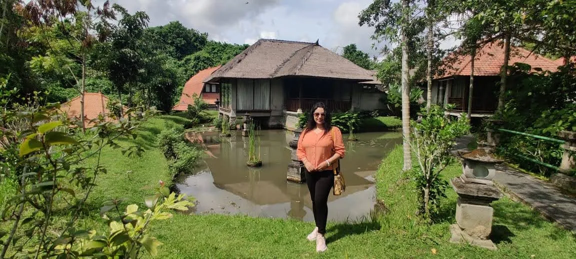 Traveler standing on green lawn before the tranquil resort pond and thatched cottages