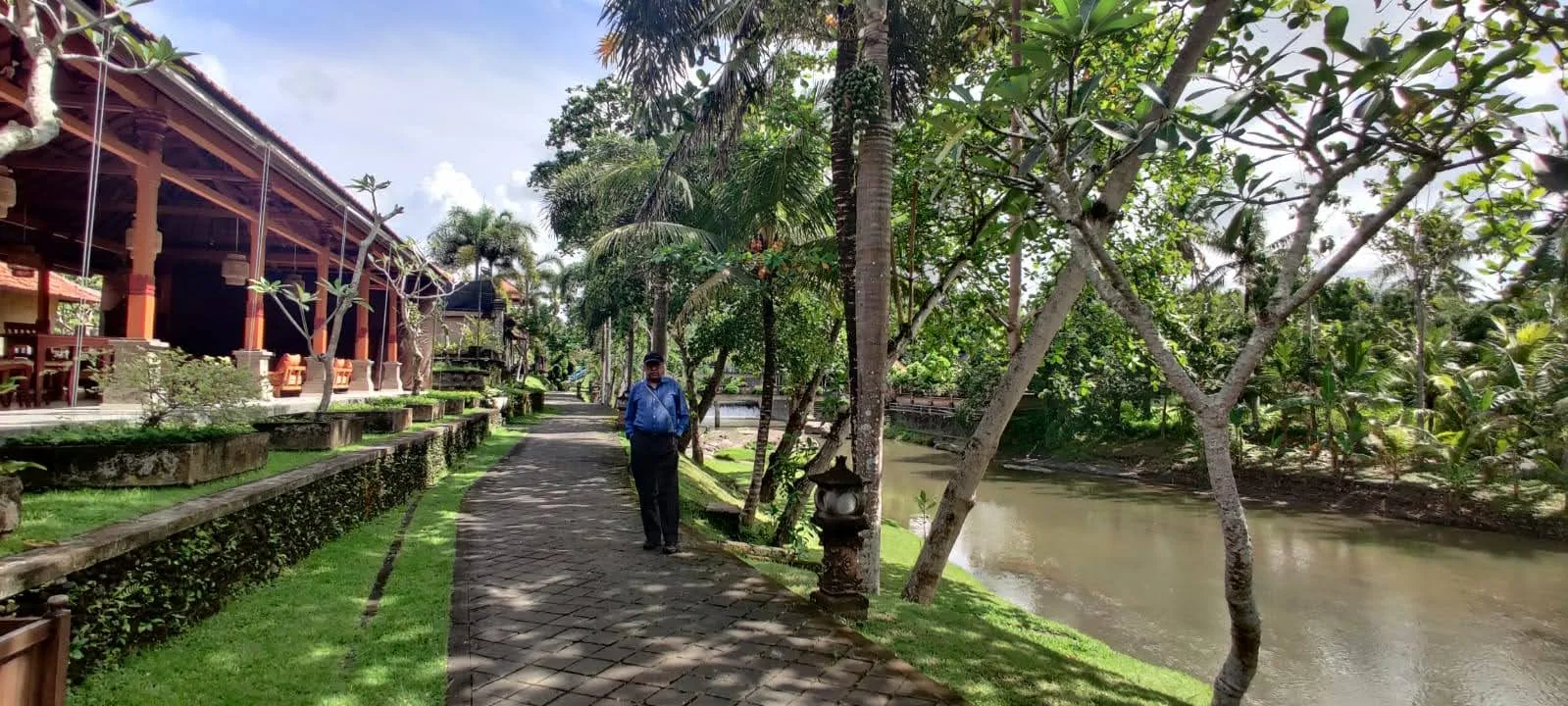 Traveler walking along the stone resort promenade beside the natural river stream and palm groves