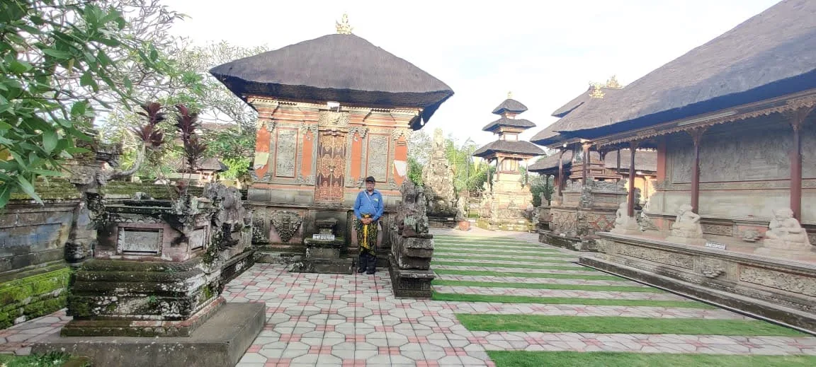Traveler standing in the inner courtyard of Batuan Temple surrounded by traditional thatched Balinese shrines and pavilions