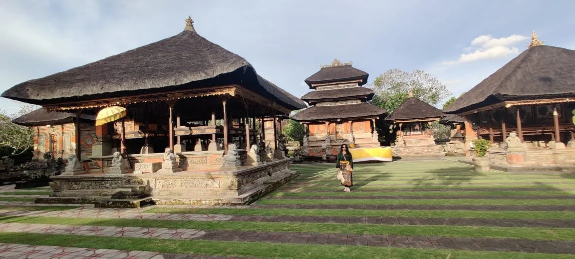 Vast green lawn courtyard of Batuan Temple surrounded by grand thatched Bale pavilions, Meru towers, and ceremonial parasols