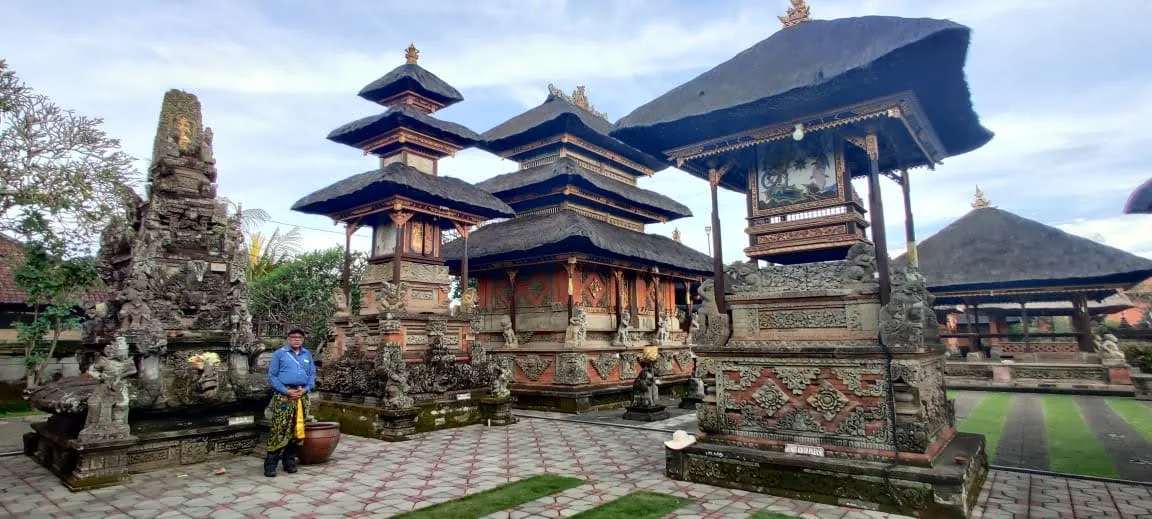 Traveler standing before the multi-tiered Meru towers with thatched roofs and brick shrines at Batuan Temple