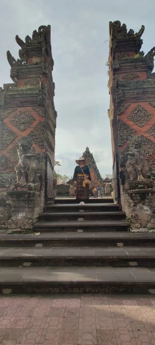 Traveler standing on the grand stone stairway between the soaring carved pillars of Batuan Temple Candi Bentar split gate