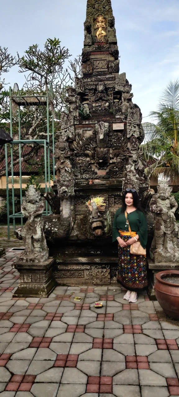 Traveler in sarong before the intricately carved stone Padmasana shrine tower and guardian statues at Batuan Temple