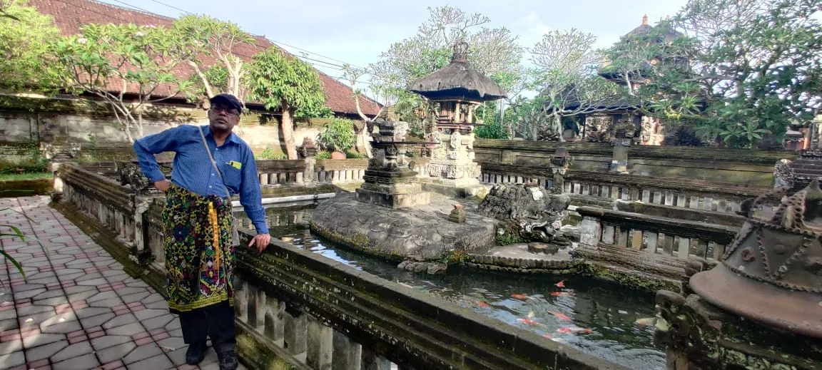 Traveler leaning against the carved stone balustrade overlooking the Bedawang Nala turtle pond and koi fish