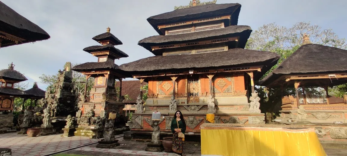 Traveler before the grand tiered sanctum pavilion with golden wood carvings, Meru roof, and yellow ceremonial drapery