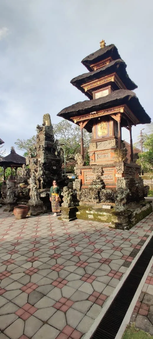 Traveler standing beside the multi-tiered Meru tower and stone carved shrines in the courtyard of Batuan Temple