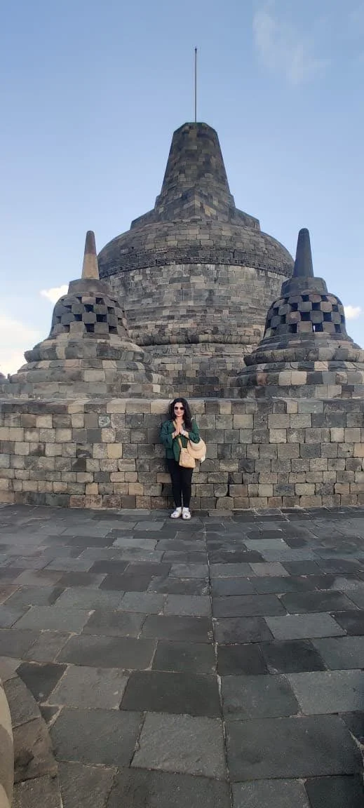 Traveler standing in namaste directly in front of the colossal Main Apex Stupa pointing into the blue sky