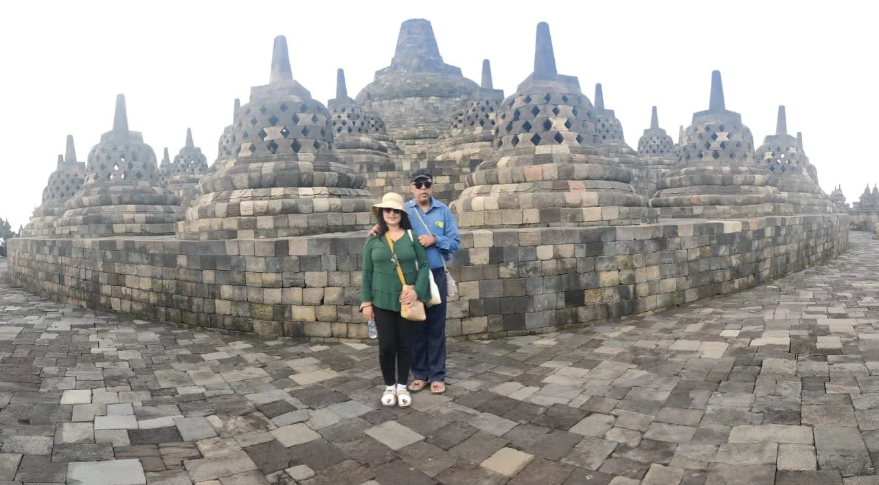 Couple centered before the concentric ring of 72 stupas spanning the upper circular terraces toward the Kedu plain