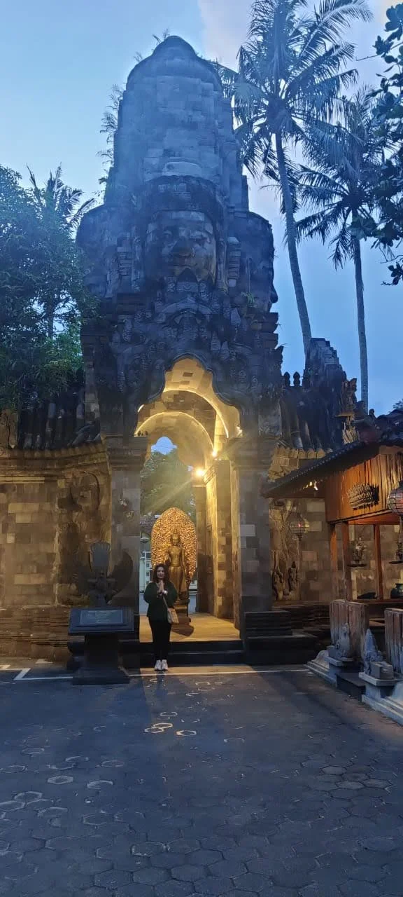 Traveler standing in namaste before the illuminated gateway arch of Vihara Mendut with golden Buddha glowing inside