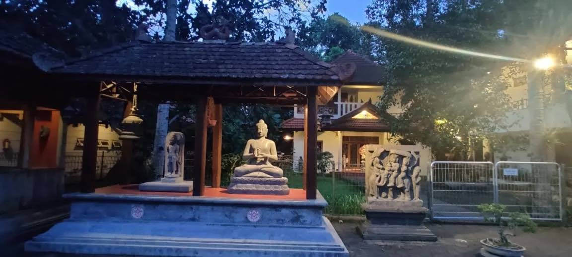 Open pavilion at Mendut with seated Buddha statue, ritual bronze bell, and ancient sculpted relief slab