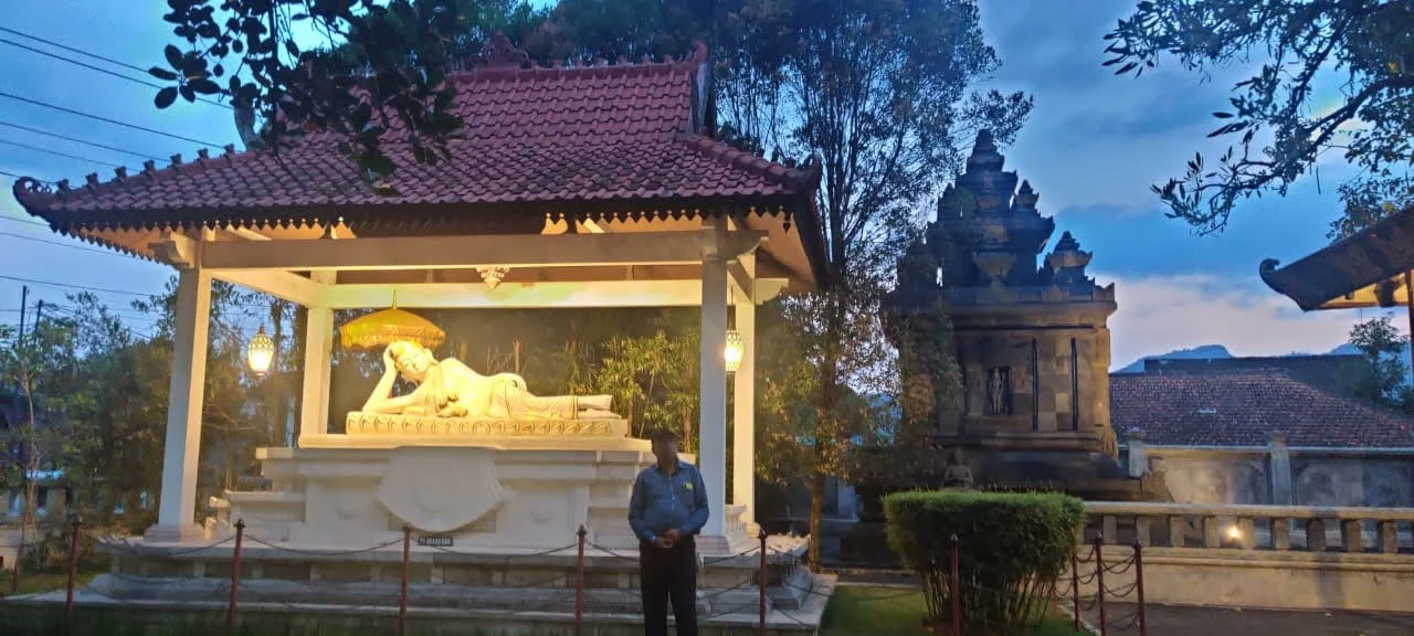 Traveler standing before the illuminated pavilion with the majestic White Reclining Buddha beneath golden parasol at Mendut