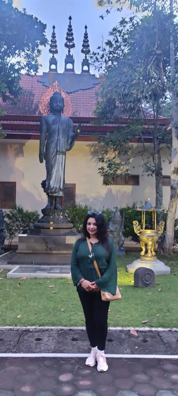 Traveler standing before standing bronze Buddha statue in Abhaya mudra with pagoda spire in monastery garden