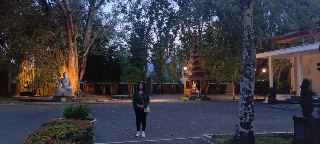 Traveler standing in the peaceful dusk courtyard of Vihara Mendut under illuminated trees and shrine