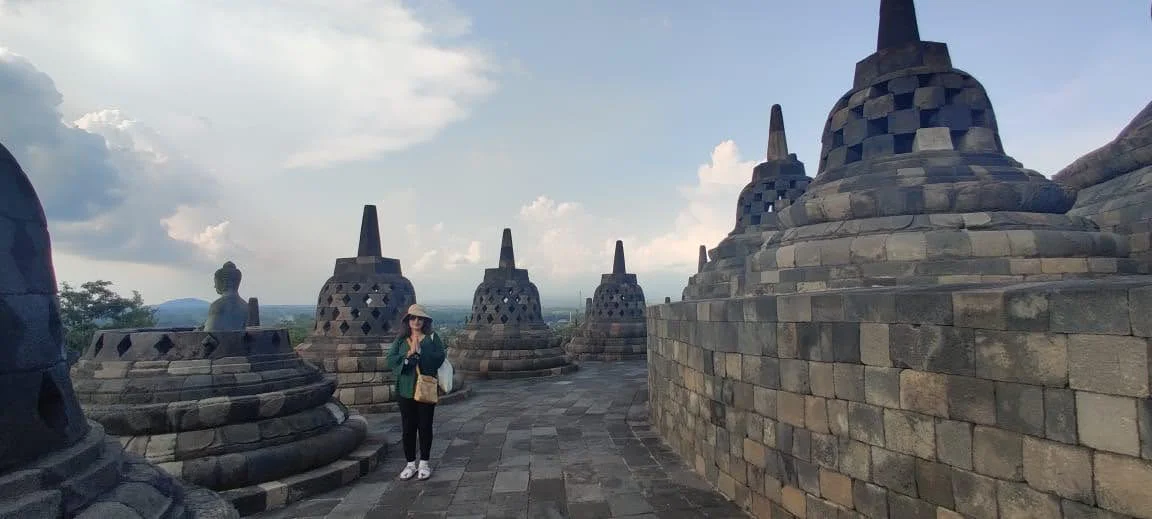 Traveler in namaste beside an open perforated stupa revealing the serene seated Buddha statue inside