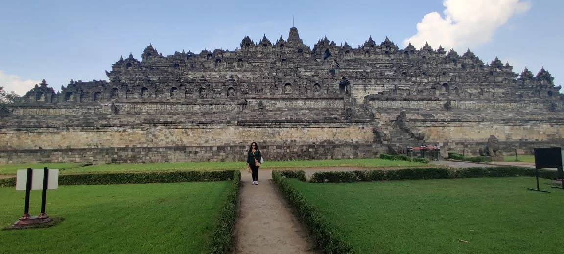 The vast tiered stone facade and terraces of Borobudur rising across the emerald grounds of Central Java