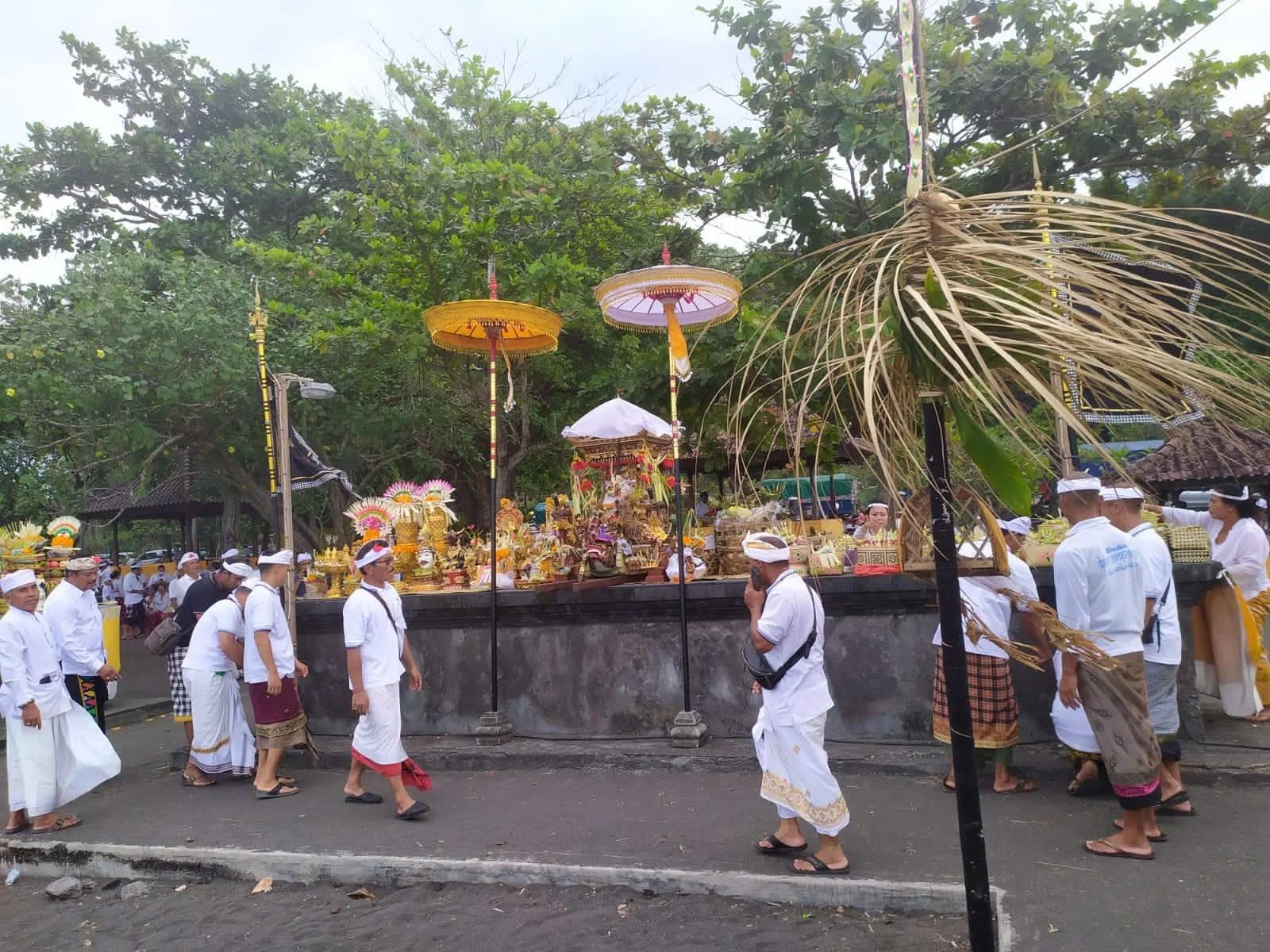 Odalan ceremony altar decorated with yellow umbrellas, fruit offerings, and worshippers in traditional white ceremonial dress