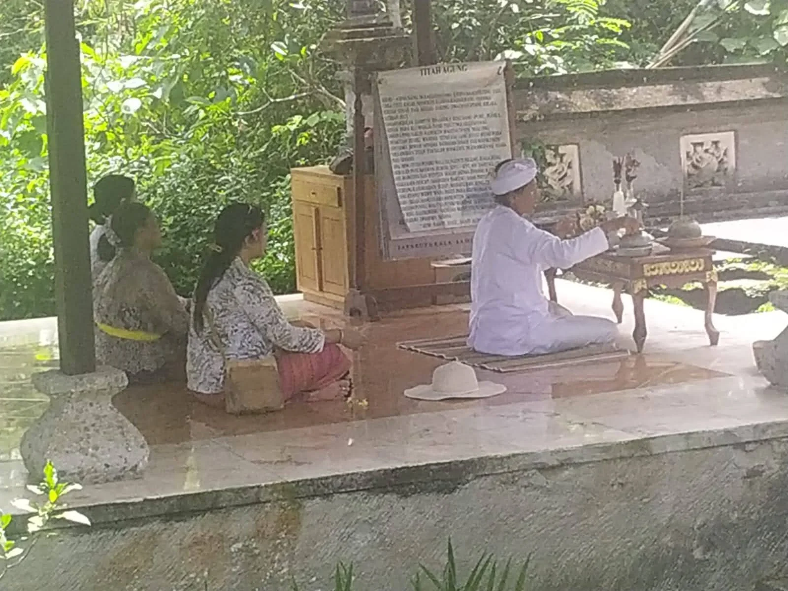 Female Balinese Hindu priest in white robes seated at the altar conducting sacred Odalan rituals with holy water