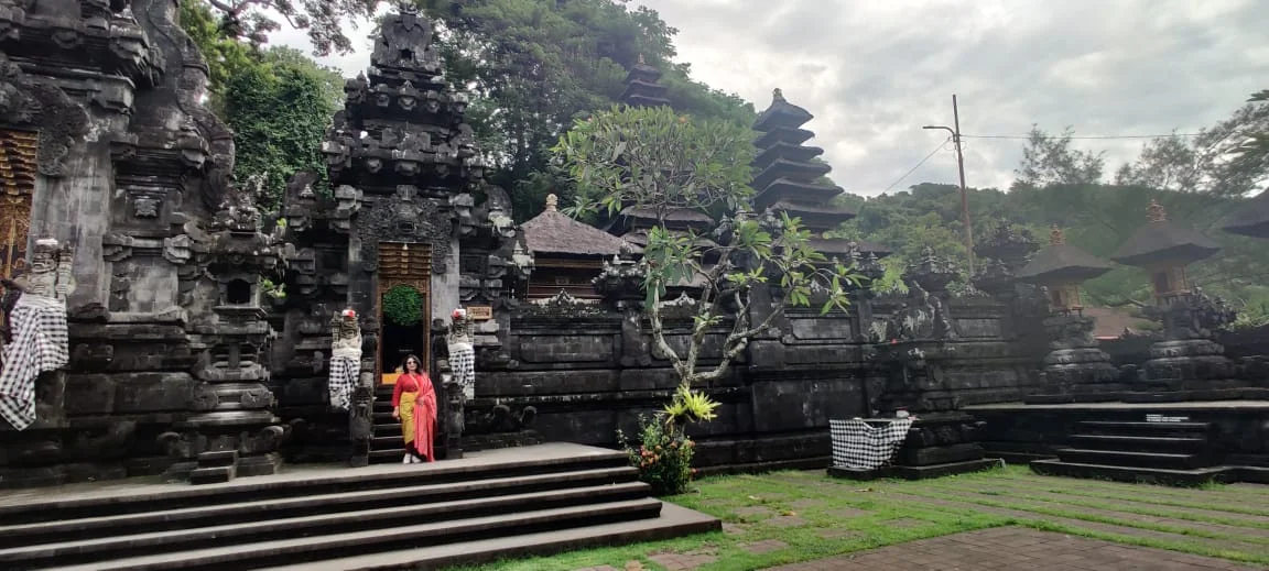 Lady traveler at the courtyard portal framed by ancient volcanic stone shrines and lush jungle hillside