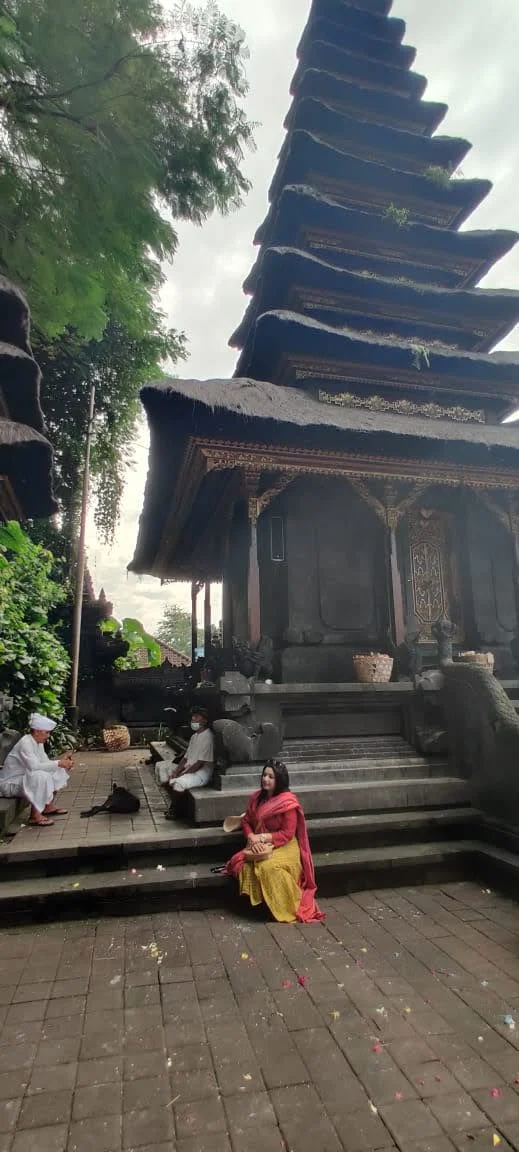Lady traveler seated on the stone steps beneath the towering 11-tiered black thatched Meru shrine tower