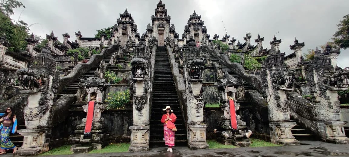 Panoramic view of lady traveler in namaste pose at the central stairway base of Pura Lempuyang