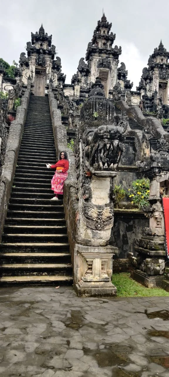 Lady traveler on grand stone staircase flanked by carved Naga dragon balustrades at Pura Penataran Agung Lempuyang