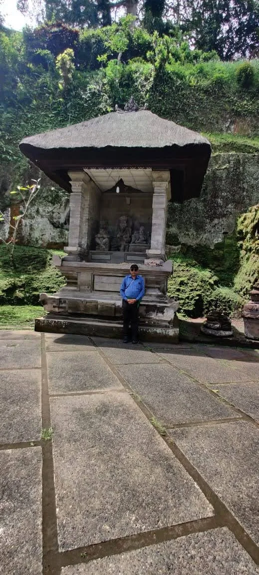 Traveler standing before an ancient thatched stone pavilion shrine preserving sacred carved deities at Goa Gajah