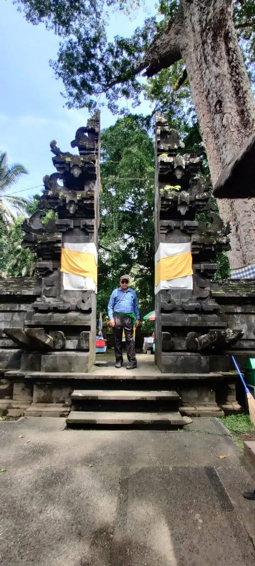 Traveler standing in the center of the monumental Candi Bentar split gate wrapped in yellow sashes at Goa Gajah
