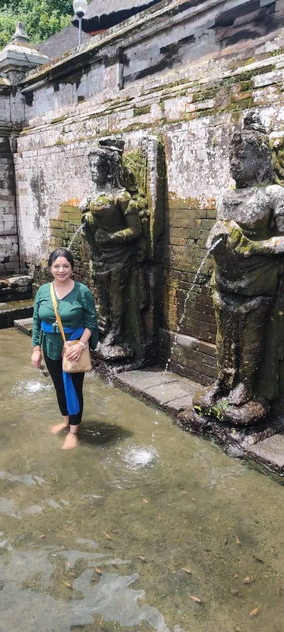 Traveler wading in the sacred Patirthaan bathing pool beside ancient stone statues of celestial maidens holding water spouts