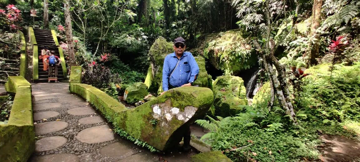 Traveler standing on the mossy carved stone bridge in the river valley behind Goa Gajah