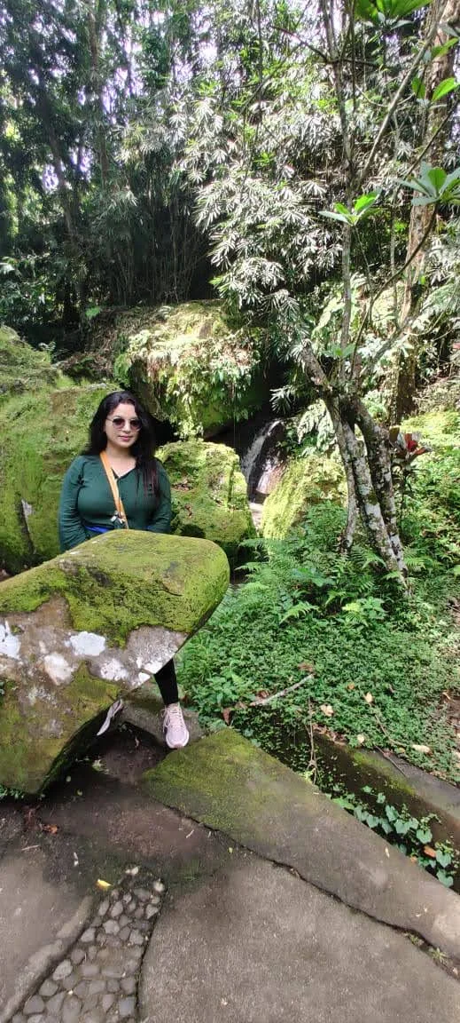 Traveler beside moss-covered stone relics and running stream waterfall in Goa Gajah forest ravine