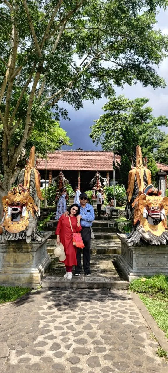 Both travelers standing between two fierce Barong lion guardian statues adorned with gold in front of the royal pavilion