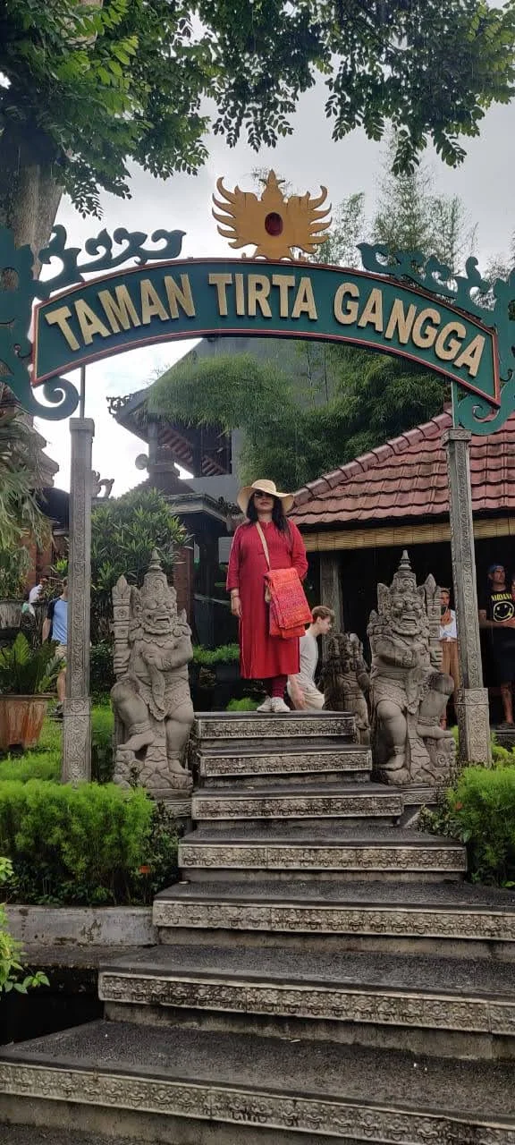 Traveler in red dress standing under the Taman Tirta Gangga entrance archway between Dvarapala stone statues
