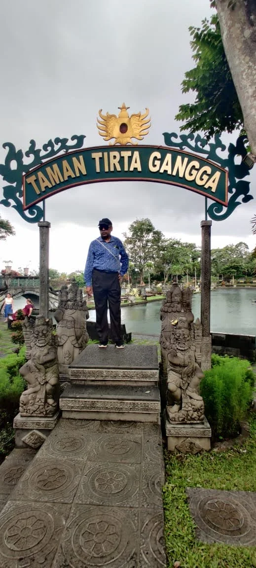 Traveler standing on the stone platform below the Taman Tirta Gangga archway beside the holy spring lake