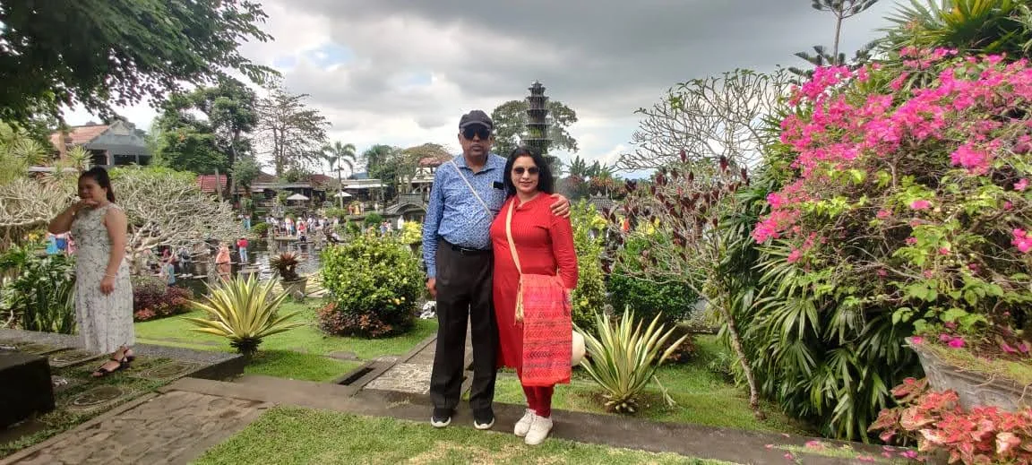 Both travelers smiling together in the tropical garden with blooming bougainvillea and the fountain tower